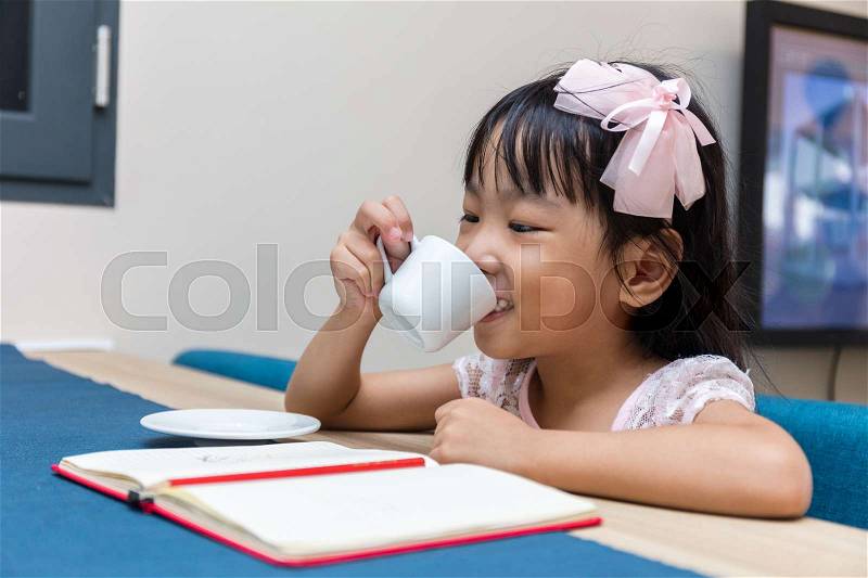 Asian little Chinese girl writing homework with coffee at home, stock photo