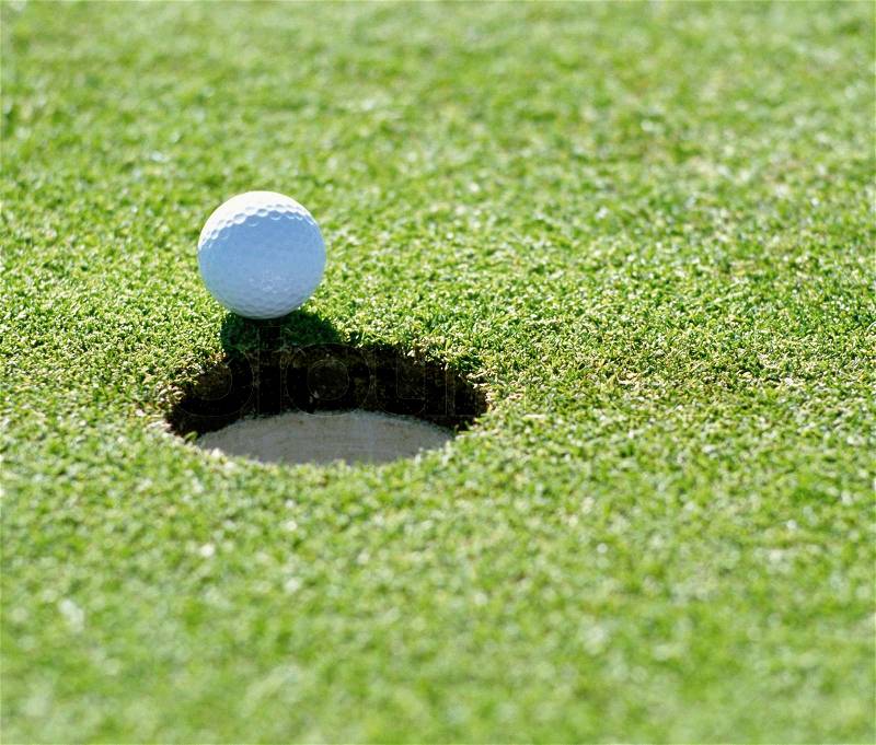 A golf ball just about to go in the hole from a long putt, stock photo