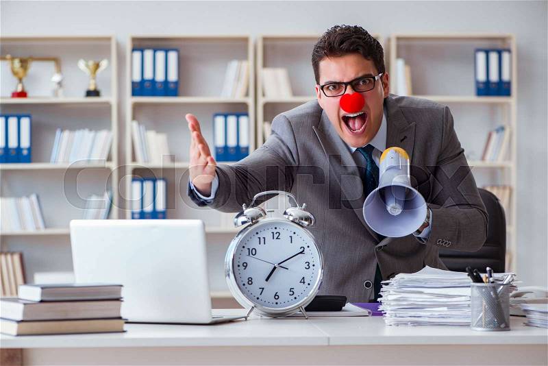 Clown businessman in the office angry frustrated with megaphone and alarm clock, stock photo