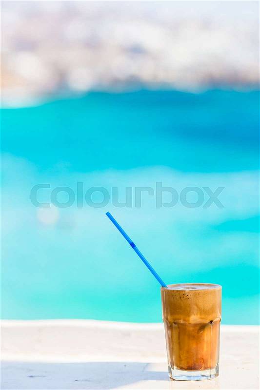 Frappe, ice coffee on the beach. Summer iced coffee frappuccino, frappe or latte in a tall glass background the sea in beach bar, stock photo