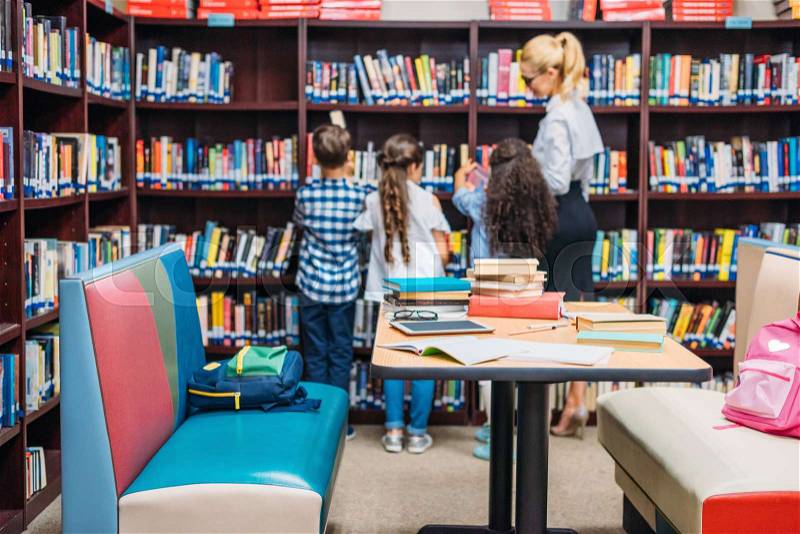 Young teacher with kids learning in library, stock photo