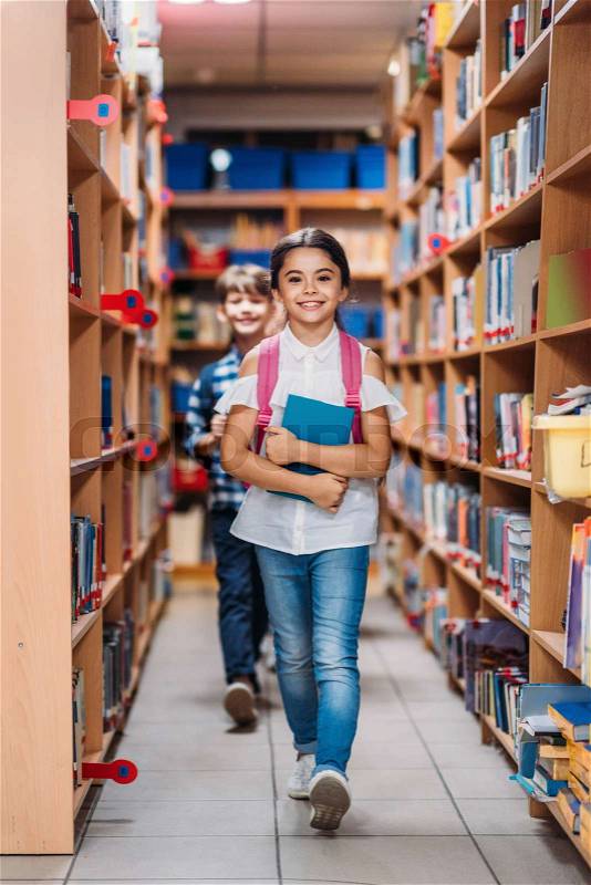 Adorable kids with books walking through library, stock photo