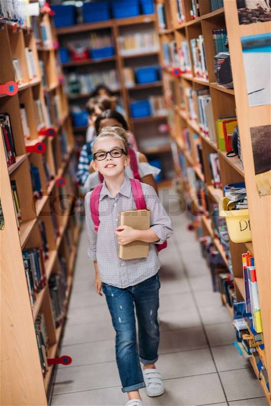 Adorable kids with books walking through library, stock photo