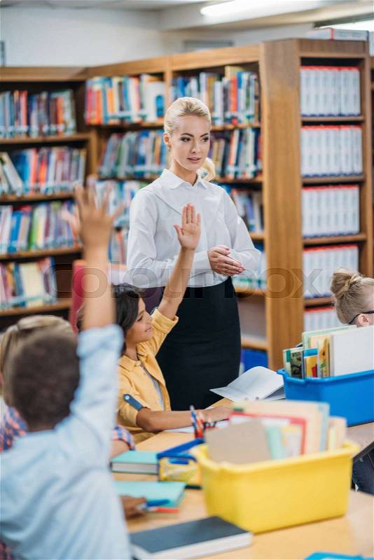 Happy young teacher giving lesson to kids in library, stock photo