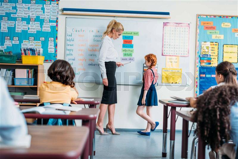 Teacher talking to adorable little schoolgirl on english lesson, stock photo