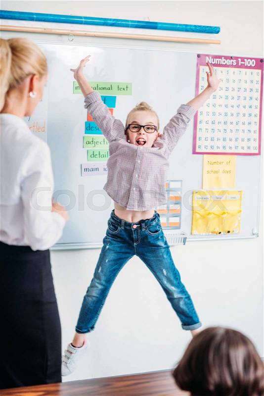 Teacher looking at adorable little jumping schoolgirl, stock photo