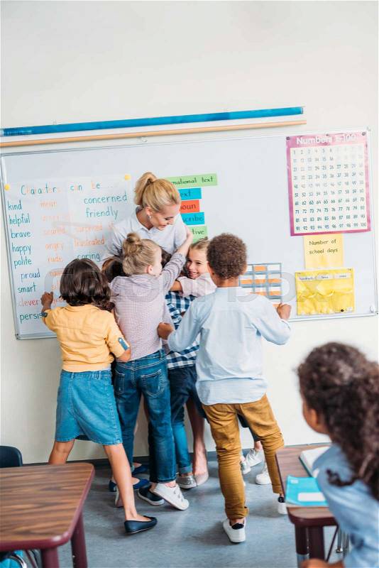 Happy young teacher embracing with pupils in class, stock photo