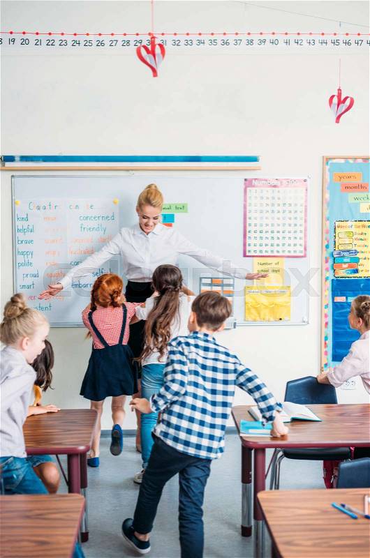 Happy young teacher embracing with pupils in class, stock photo