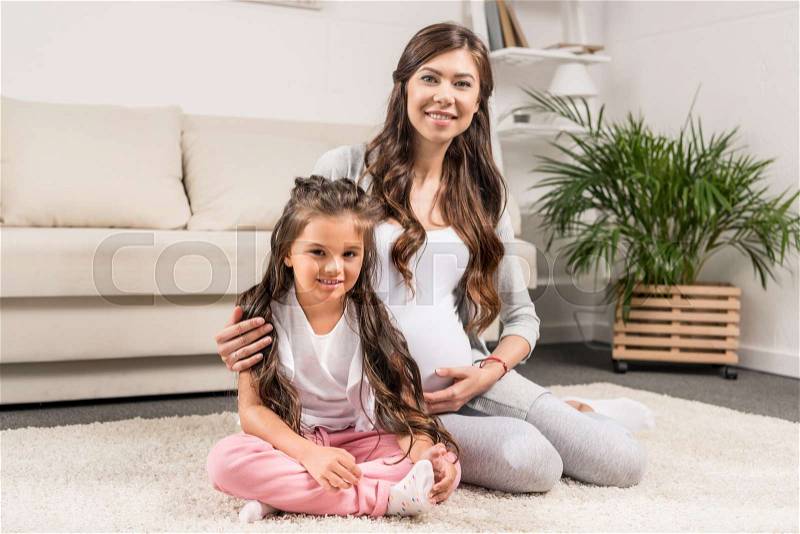 Pregnant woman sitting on a furry rug with her little daughter, stock photo