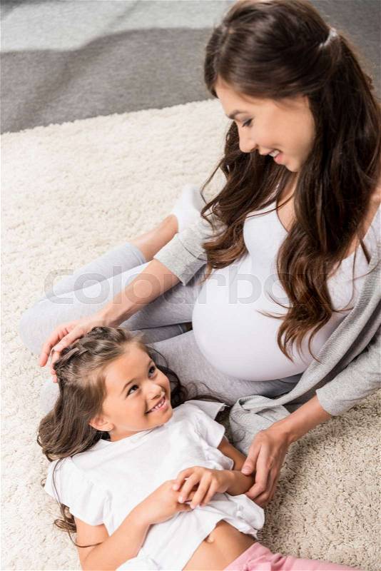 Pregnant woman sitting on a furry rug with her little daughter lying in her lap, stock photo