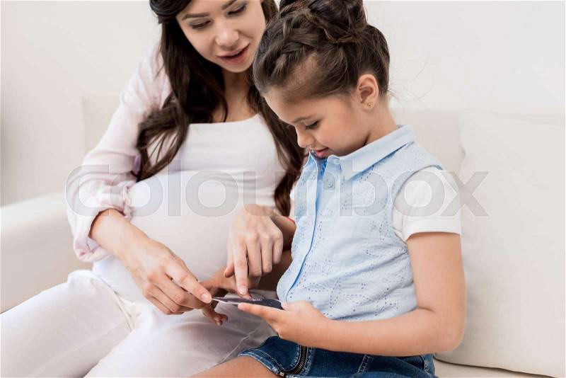 Little girl looking at pregnancy ultrasound photo with her mother, stock photo