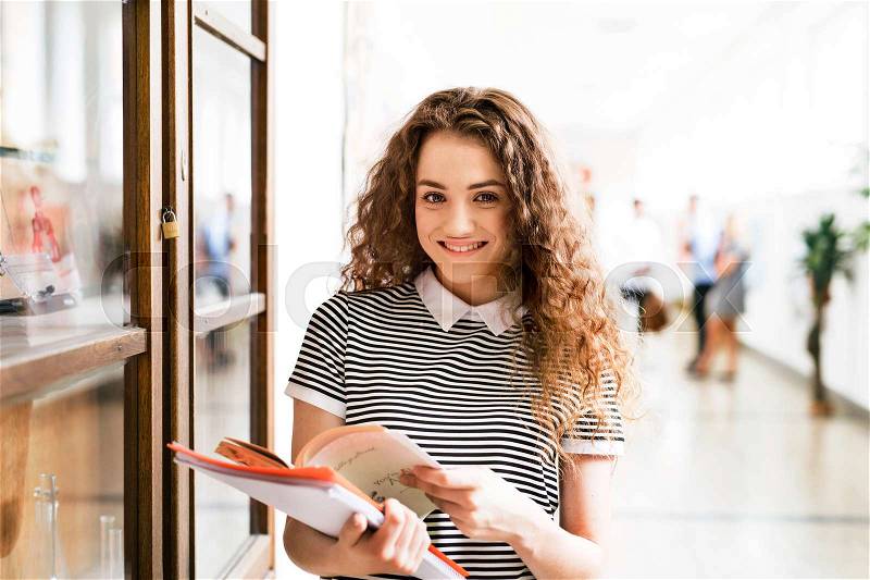 Attractive teenage girl with notebooks in high school hall during break, stock photo