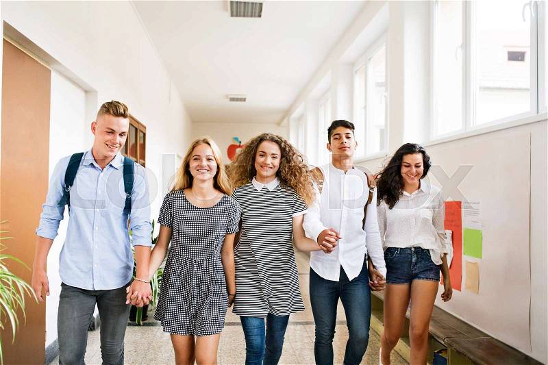 Group attractive teenage students walking in high school hall, holding hands, stock photo