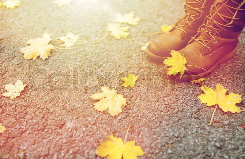 Season, footwear and people concept - female feet in boots with autumn leaves on ground, stock photo