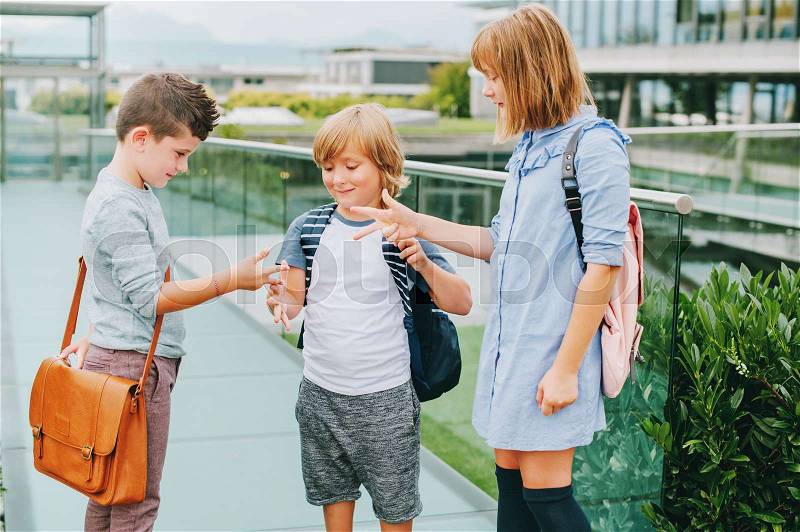 Group of 3 kids playing Rock, Paper, Scissors game on schoolyard. Back to school concept, fashion for children, stock photo