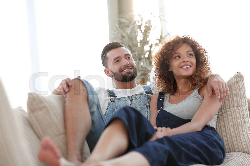 Young couple in work clothes sitting on couch in new house, stock photo