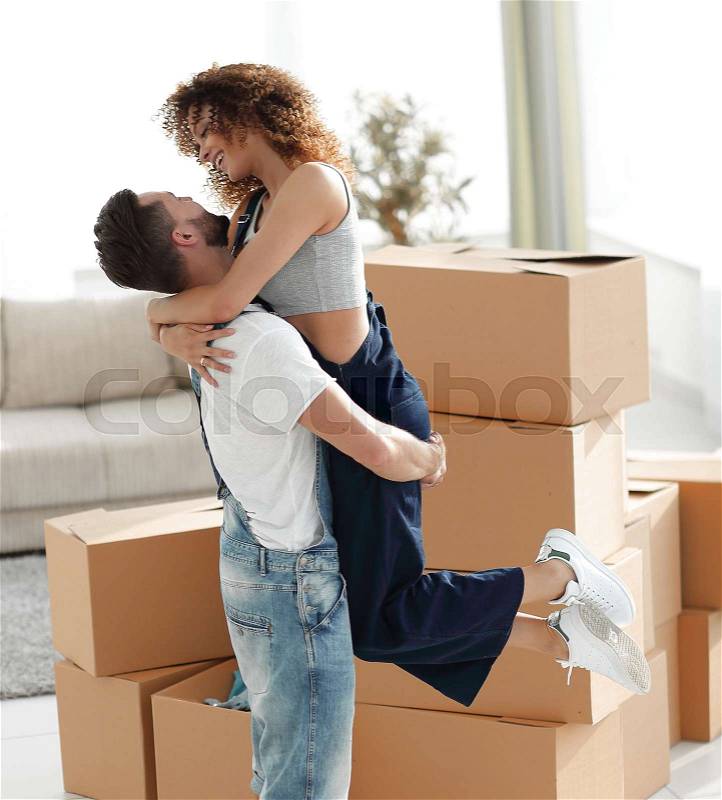 Husband hugs a happy wife against the background of large cardboard boxes, stock photo