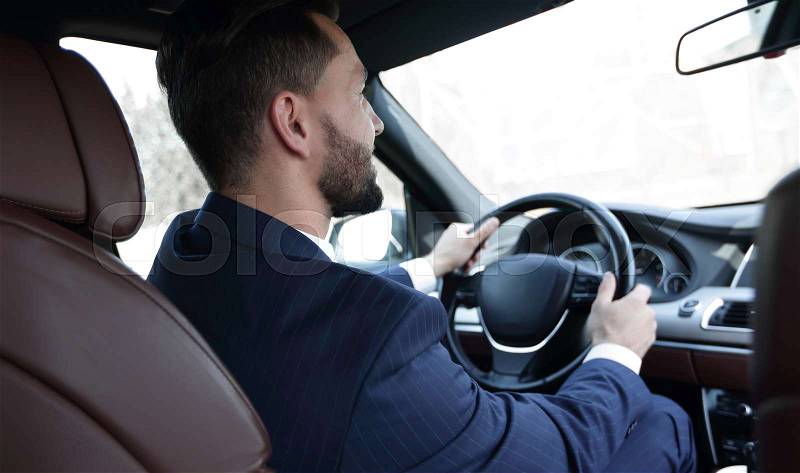 Confident businessman sits at the wheel in his car and looks at the road. Lifestyle, stock photo