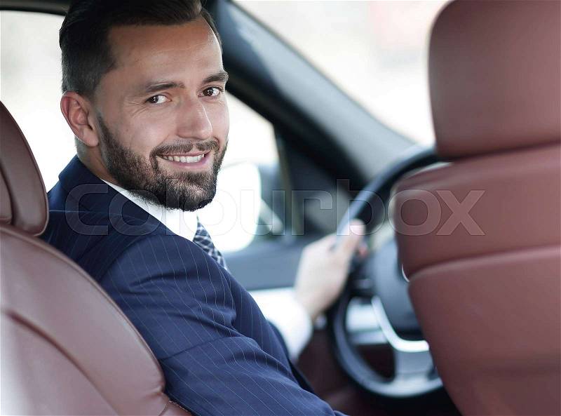 Successful businessman sitting at the wheel of a car and looking at the camera, stock photo