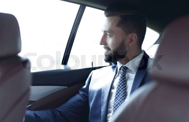 Smiling successful man sitting in the back seat of a car, stock photo