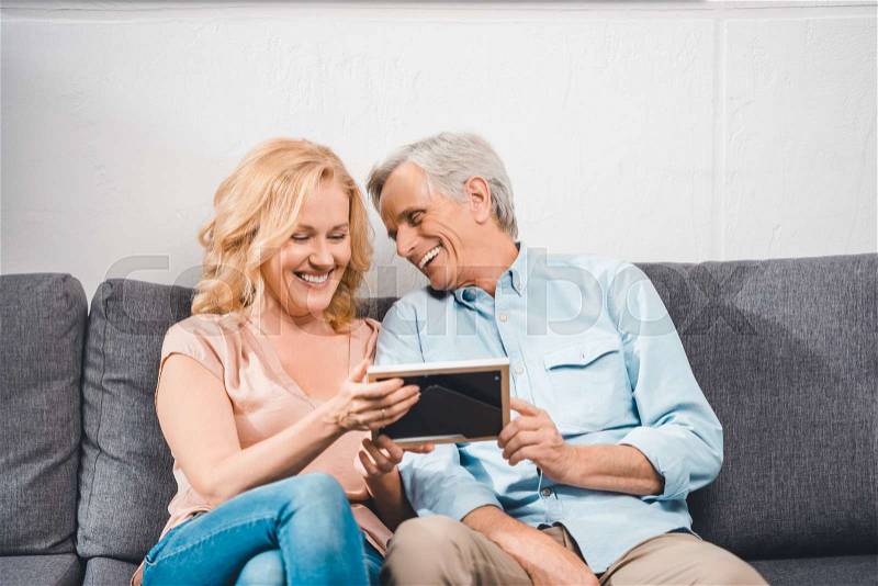 Happy wife and husband looking at photo frame at home, stock photo