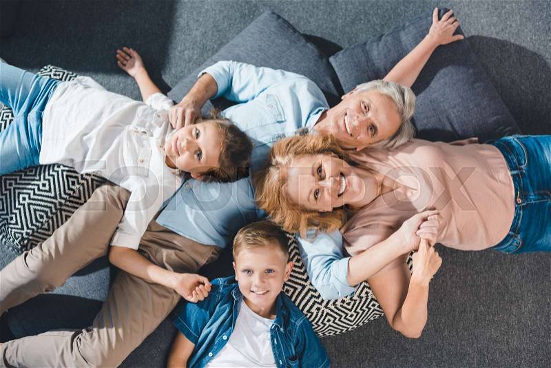 Top view of happy grandparents and grandchildren lying on floor and looking at camera, stock photo