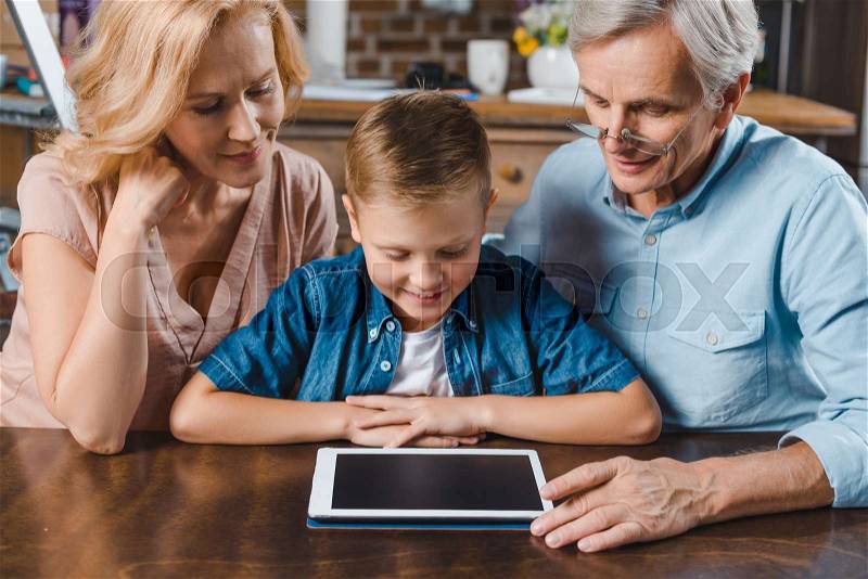 Grandparents and grandson using digital tablet at home, stock photo