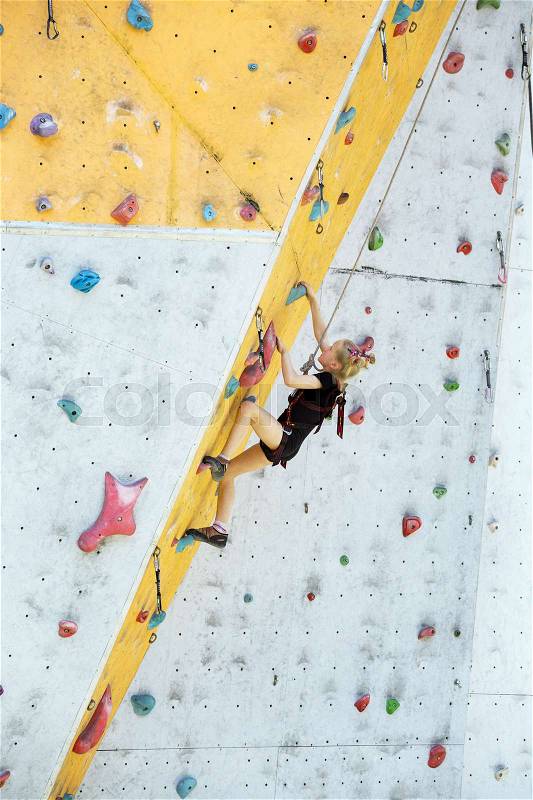 Bouldering, little girl climbing up the wall and climber multicolored grips. Leisure activity , stock photo