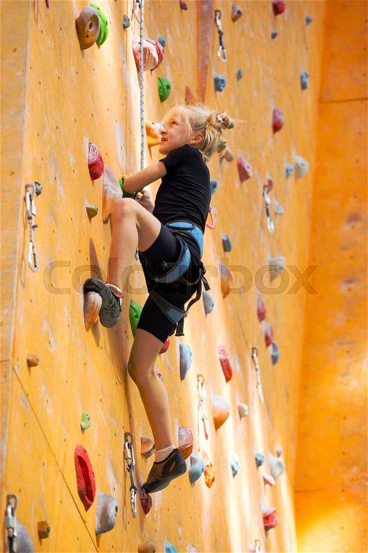 Bouldering, little girl climbing up the wall and climber multicolored grips. Leisure activity , stock photo