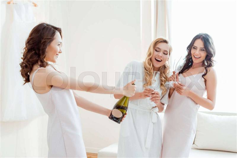 Beautiful happy bride with bridesmaids opening champagne bottle, stock photo
