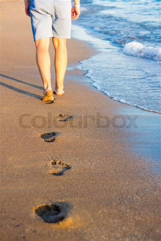 Summer and vacation concept - walking man and footprints on the sunset beach in warm country, stock photo