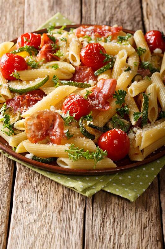 Italian cuisine: penne pasta with fried prosciutto, cherry tomatoes, zucchini and cheese close-up on a plate. vertical , stock photo