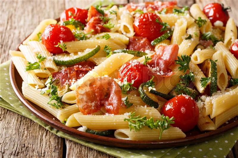 Italian penne pasta with ham prosciutto, tomato, zucchini and parmesan close-up on a plate. horizontal , stock photo
