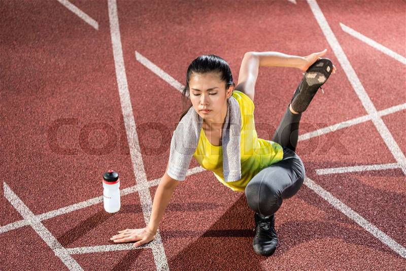 Woman sprinter doing warm up exercise before sprint outdoors, stock photo