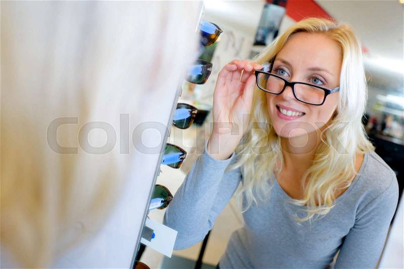 Beautiful young woman trying new glasses at optician store, stock photo