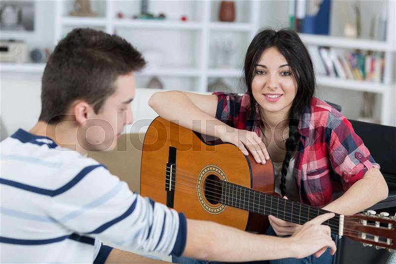 Young man teaches his girlfriend to play the guitar indoors, stock photo