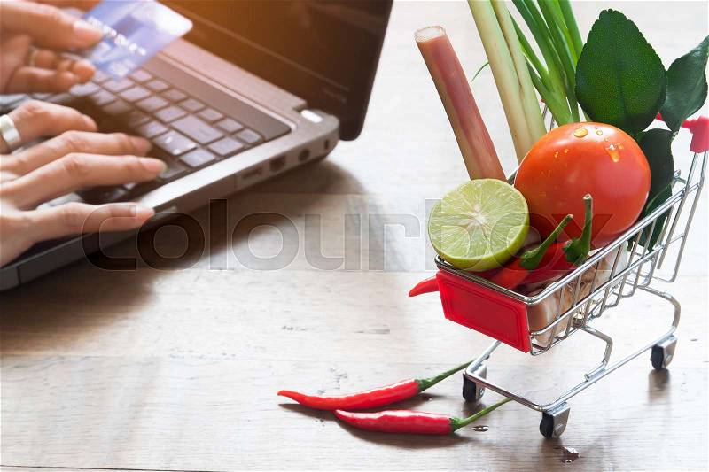 Shopping cart with full of fresh vegetables from market, Shopping online concept with woman using laptop and credit card in background, stock photo