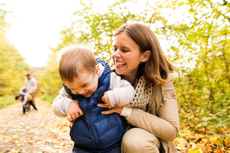 Beautiful young mother with her son and whole family in warm clothes on a walk outside in colorful autumn nature, stock photo