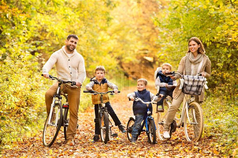Beautiful young family with three sons in warm clothes cycling outside in autumn nature, stock photo