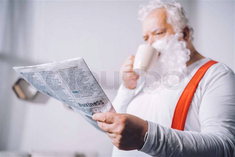 Selective focus of santa claus drinking coffee while reading newspaper, stock photo