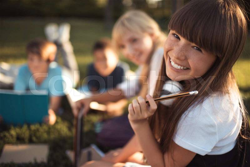 Portrait of beautiful happy teenage girl holding pencil and smiling at camera, stock photo