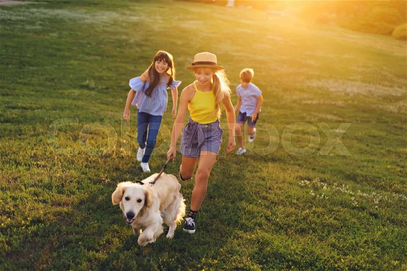 Happy teenagers with cute golden retriever dog walking in park, stock photo