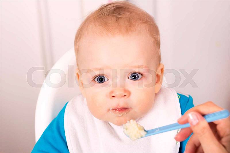 Cute blue-eyed baby boy eating porridge. one year sonMother feeding her adorable one year son, stock photo