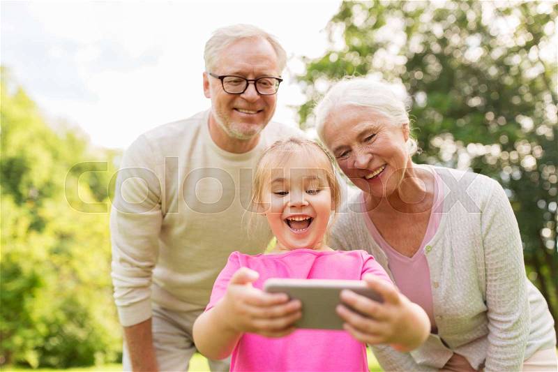 Family, generation and people concept - happy smiling grandmother, grandfather and little granddaughter taking selfie by smartphone at park, stock photo