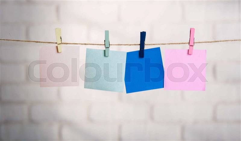 Wooden clothespin and blank paper on a rope against white brick wall, stock photo