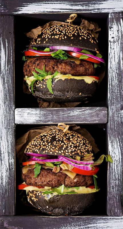 Black big sandwich - black hamburger with juicy beef burger, cheese, tomato, and red onion in box on black background. Flat lay. Top view, stock photo