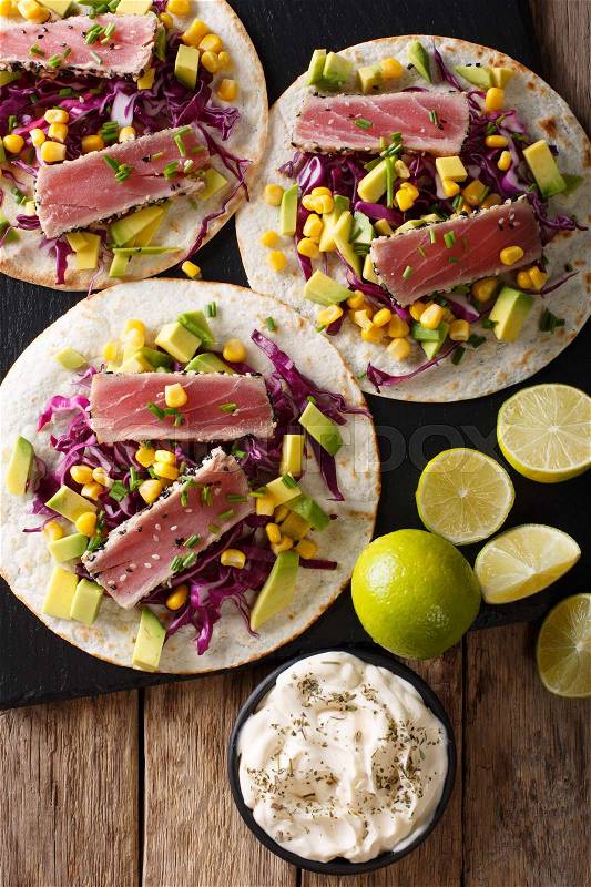 Mexican tacos with tuna, red cabbage, corn, avocado and onions close-up on the table. Top view from above vertical , stock photo