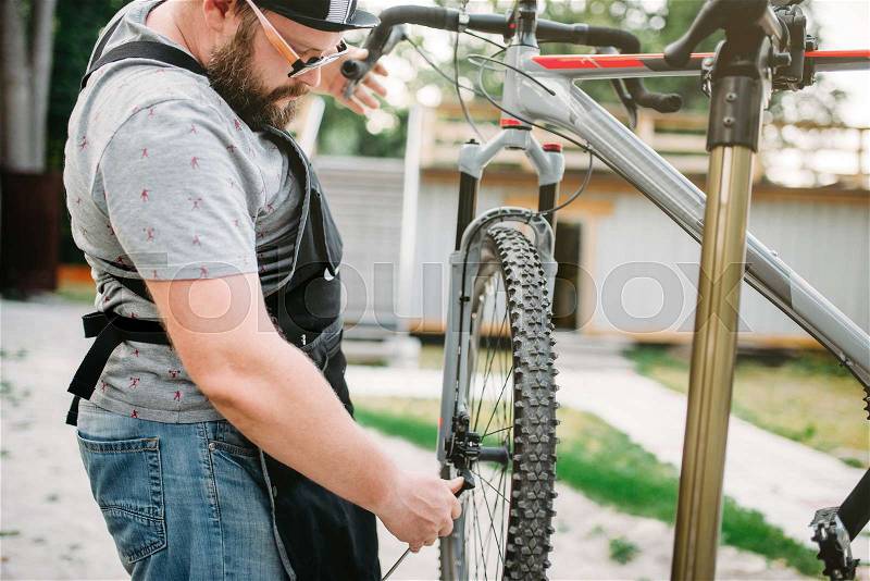 Professional bicycle mechanic in apron adjusts bike. Cycle workshop outdoor. Bicycling sport, bearded service man work with wheel, stock photo