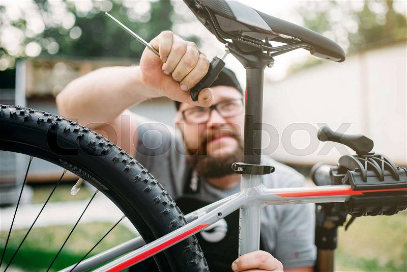 Bicycle mechanic adjusts with service tools bike seat. Cycle workshop outdoor. Bicycling sport, repairman at work, stock photo