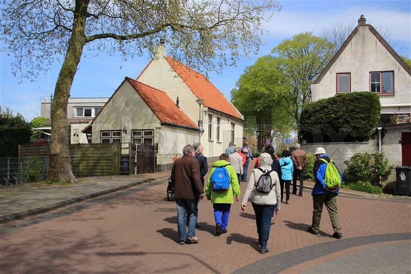 The tourists are walking with the guide through the residential area of the village Abbenbroek in the beautiful spring, stock photo